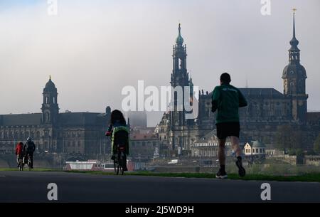 Dresde, Allemagne. 26th avril 2022. La tour de l'hôtel de ville est encore enveloppée de brouillard le matin tandis que les cyclistes et un jogger sont sur le sentier de l'Elbe en face de la vieille ville avec le Ständehaus (l), la Hofkirche et la tour de l'hôtel de ville (r). Crédit : Robert Michael/dpa/Alay Live News Banque D'Images