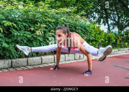 Tenue sportive jeune femme faisant de l'exercice de la main dans la posture de feu. Athlète féminine s'pratiquant dans le parc Banque D'Images