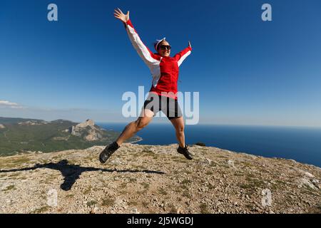 Une femme heureuse saute sur un sommet d'une montagne en été dans les montagnes appréciant la montée avec de beaux rochers et fond de mer Banque D'Images
