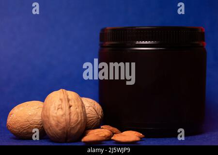 bocal noir avec noix sur fond bleu. Banque D'Images