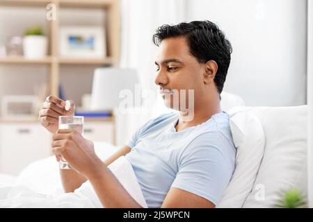 homme au lit tombant le médicament dans un verre d'eau Banque D'Images