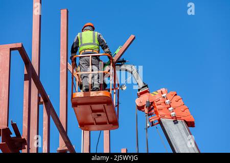 Les constructeurs masculins travaillent en hauteur dans un berceau de levage, créant le cadre en fer du bâtiment. Banque D'Images