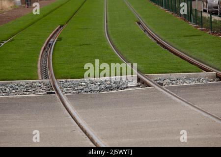 Les rails passent sur la route puis la pierre pour finir sur l'herbe verte guidant le regard. Banque D'Images