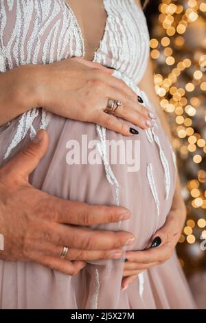 Les mains des hommes et des femmes embrassent le ventre de la fille enceinte. En attente d'un petit miracle Banque D'Images