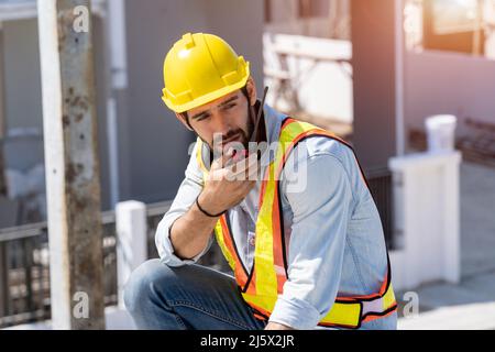 Le travailleur du génie de la construction parle à la radio, l'ingénieur de la construction utilise la communication radio sur le chantier de construction. Banque D'Images