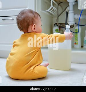 Bébé garçon joue avec des détergents et des produits de nettoyage dans une armoire de cuisine ouverte. Problèmes de sécurité des enfants dans la chambre d'accueil, petit enfant Banque D'Images