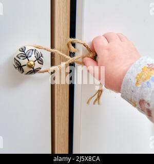 Bébé garçon se déporte d'un tiroir de cabinet avec sa main. L'enfant tient la poignée de la porte de l'armoire, petit enfant Banque D'Images