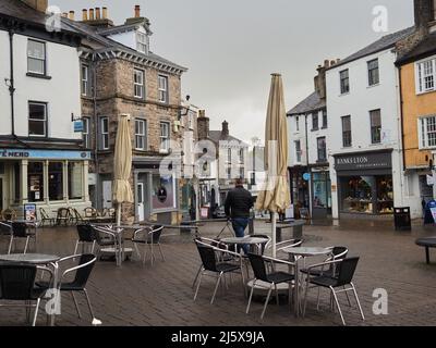 Un homme qui marche devant des tables et des chaises vides d'un café extérieur lors d'une journée humide à Kendal, Cumbria, Royaume-Uni Banque D'Images