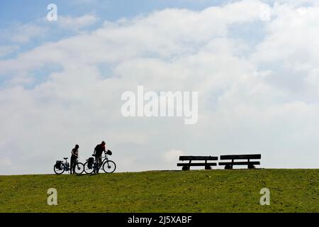 Les derniers mètres, deux cyclistes poussent leurs vélos sur une crête de digue à deux bancs, le parc national de la mer des Wadden du Schleswig-Holstein, Westerhever, Schleswig Banque D'Images