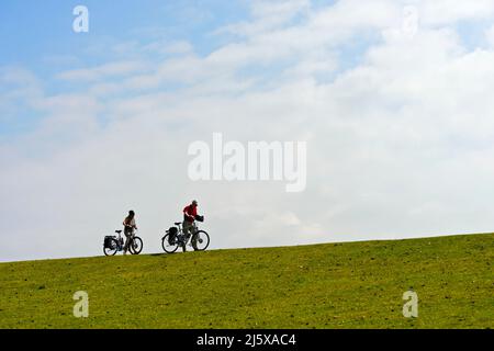 Deux cyclistes poussent leurs vélos sur une crête de digue, Parc national de la mer des Wadden du Schleswig-Holstein, Westerhever, Schleswig-Holstein, Allemagne Banque D'Images