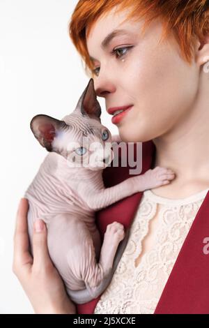 Hipster jeune femme rouge embrassant doucement Canadian Sphynx Cat Mise au point sélective sur le chaton, faible profondeur de champ. Femme mignonne vêtue d'une veste rouge Banque D'Images