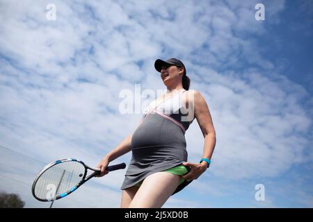 Femme enceinte en robe jouant au tennis sous le ciel ensoleillé Banque D'Images
