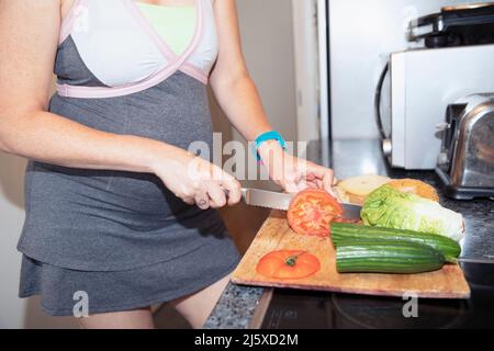 Femme enceinte qui coupe des légumes à la planche à découper dans la cuisine Banque D'Images