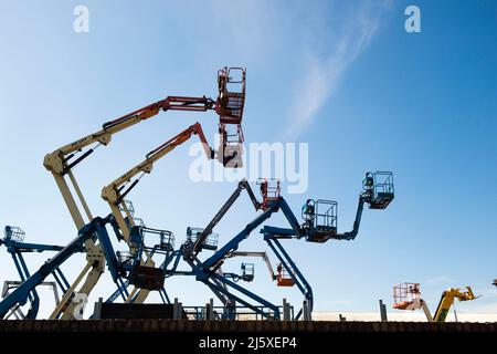 Les cueilleurs de cerisier ont silhoueté agaianst un ciel bleu sur un domaine industriel près de Lincoln, Royaume-Uni.plates-formes élévatrices mobiles de travail (MEWPs), ou autrement connu sous le nom Banque D'Images