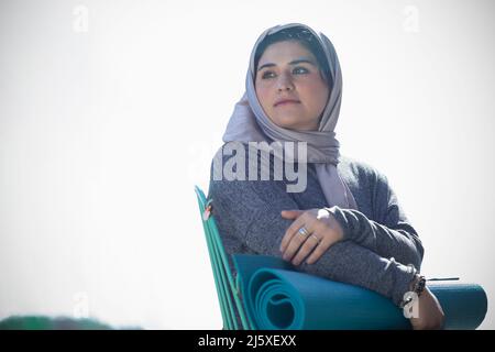 Jeune femme réfléchie en hijab avec tapis de yoga Banque D'Images