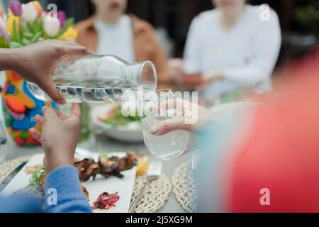 Gros plan homme versant l'eau de la carafe à la table de patio Banque D'Images