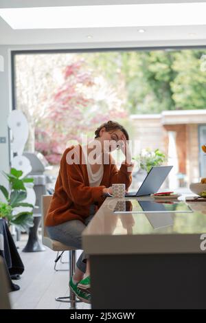 Femme stressée travaillant de la maison à l'ordinateur portable dans la cuisine Banque D'Images