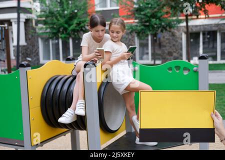 deux jeunes filles de charme dans des vêtements identiques avec des smartphones à l'extérieur. les enfants surfent sur le net. addiction de smartphone. les enfants dans les réseaux sociaux. textinin Banque D'Images