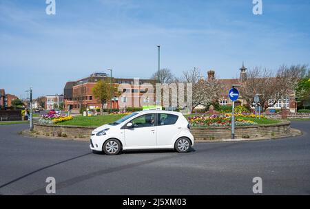 Voiture se rendant autour d'un petit rond-point parrainé par les Britanniques sur une route en Angleterre, au Royaume-Uni. Banque D'Images