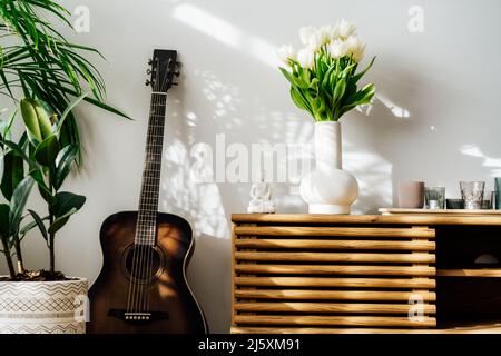 Décoration intérieure minimaliste scandinave - bouquet de fleurs de tulipe blanches dans un vase, bougies, statuette de Bouddha sur une armoire en bois. Plante de maison verte Banque D'Images