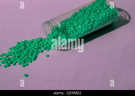 De magnifiques granules de cire verte avec extrait d'aloès pour l'épilation sont versés sur un fond violet clair, à partir d'un pot transparent. Épilation, épilation Banque D'Images