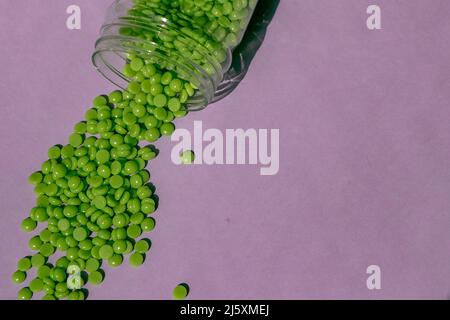 De magnifiques granules de cire verte avec extrait d'aloès pour l'épilation sont versés sur un fond violet clair, à partir d'un pot transparent. Épilation, épilation Banque D'Images