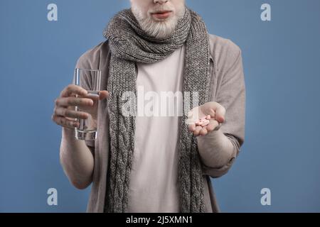 Vue rognée de l'homme prenant des pilules, tenant un verre d'eau douce sur fond bleu studio, rognée, gros plan Banque D'Images