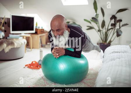 Homme mûr avec la barbe s'exerçant avec le ballon de fitness à la maison Banque D'Images