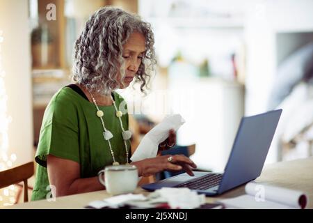 Femme âgée avec des reçus bancaires sur ordinateur portable Banque D'Images