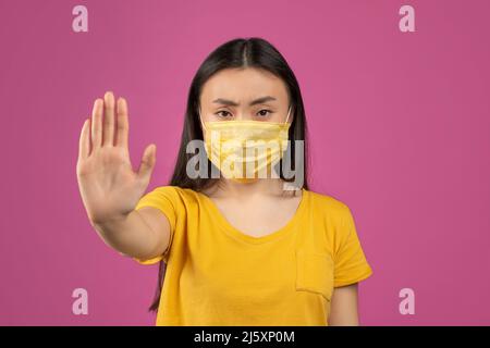 Arrêter la pandémie de Covid-19. Jeune femme asiatique portant un masque de protection médical et une main éstretching, fond violet Banque D'Images