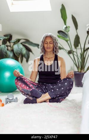 Femme sereine méditant dans la position de lotus à la maison Banque D'Images