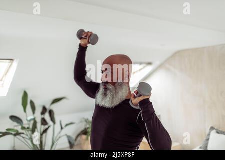 Homme mûr avec la barbe s'exerçant avec des haltères à la maison Banque D'Images