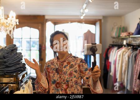 Une femme propriétaire de boutique se vjournalisation avec un smartphone dans une boutique de vêtements Banque D'Images