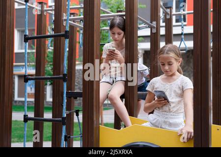 deux jeunes filles de charme dans des vêtements identiques avec des smartphones à l'extérieur. les enfants surfent sur le net. addiction de smartphone. les enfants dans les réseaux sociaux. textinin Banque D'Images