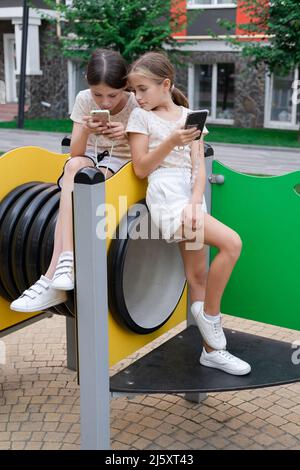 deux jeunes filles de charme dans des vêtements identiques avec des smartphones à l'extérieur. les enfants surfent sur le net. addiction de smartphone. les enfants dans les réseaux sociaux. textinin Banque D'Images