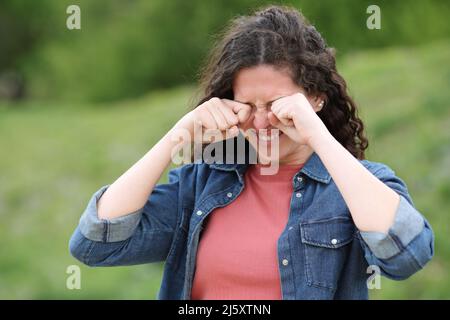 Femme stressée se grattant les yeux qui démangent debout dans un parc vert Banque D'Images