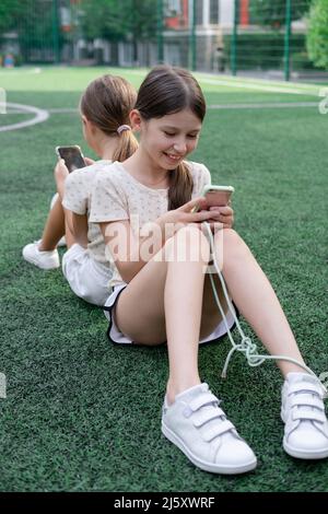 deux jeunes filles de charme dans des vêtements identiques avec des smartphones à l'extérieur. les enfants surfent sur le net. addiction de smartphone. les enfants dans les réseaux sociaux. textinin Banque D'Images