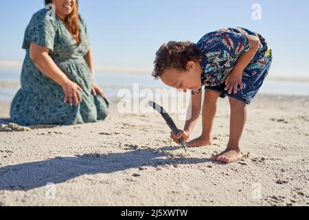 Garçon avec le syndrome de Down dessin dans le sable avec bâton sur la plage ensoleillée Banque D'Images