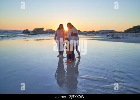 La famille se coud dans le sable humide sur la plage de l'océan au coucher du soleil Banque D'Images