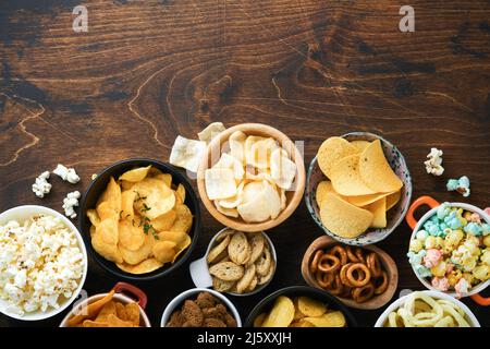 Aliments ou collations malsains. Tous les en-cas classiques de pommes de terre avec des arachides, du pop-corn et des rondelles d'oignon et des bretzels salés dans des assiettes à bol sur fond de bois ancien. Banque D'Images