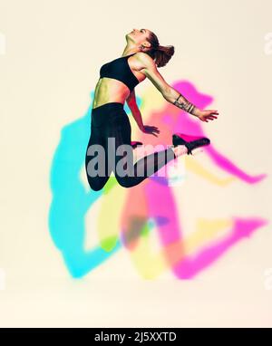 Femme sportive qui saute dans la silhouette. Photo de femme musclée en noir sportswear sur fond blanc avec effet des ombres de couleurs rvb. Mouvement dynamique Banque D'Images