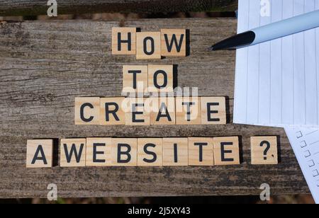 Comment créer un site Web? Lettres majuscules noires sur blocs de jouets en bois sur fond de table de jardin naturel avec papier et crayon. Banque D'Images