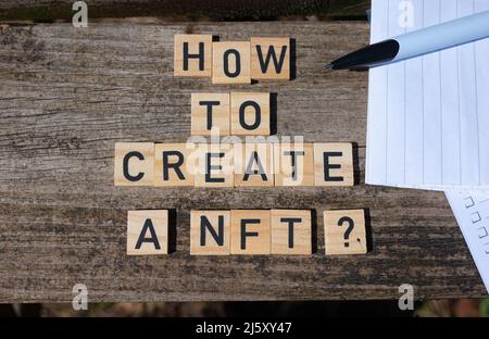 Comment créer une NFT ? Lettres majuscules noires sur blocs de jouets en bois sur fond de table de jardin naturel avec papier et crayon. Parfait pour les sites Web. Banque D'Images