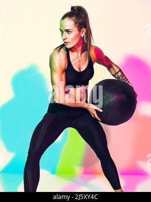 Femme forte faisant un exercice de torsion avec le ballon de med. Photo de femme avec un physique parfait sur fond blanc avec effet des ombres de couleurs rvb. Force Banque D'Images