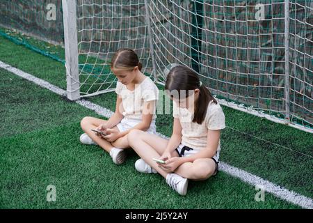 deux jeunes filles de charme dans des vêtements identiques avec des smartphones à l'extérieur. les enfants surfent sur le net. addiction de smartphone. les enfants dans les réseaux sociaux. textinin Banque D'Images