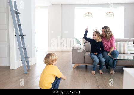 Mère pieds nus avec fille assise ensemble sur un canapé confortable tout en jouant avec son fils dans le salon léger à la maison Banque D'Images