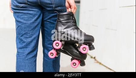 Vue latérale d'une femme courte en denim qui tient des patins à roulettes tout en marchant près d'un mur de tuiles dans la rue Banque D'Images