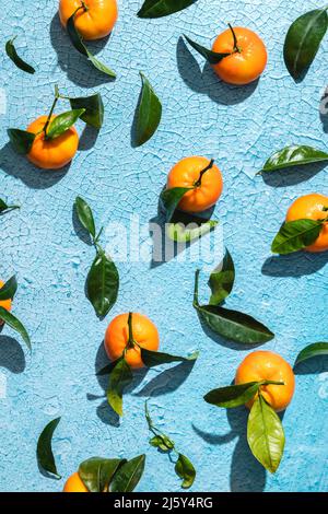 Vue de dessus fond plein cadre de mandarines tropicales mûres avec des tranches de feuilles et la peau sur une surface bleu vif craquelée Banque D'Images