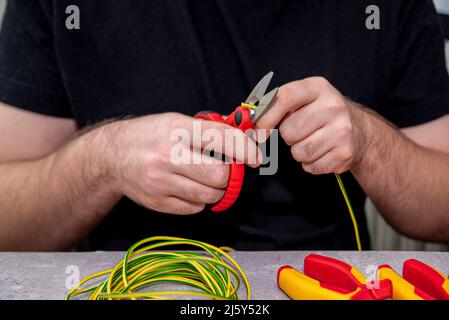 un homme tenant un couteau électrique pour dénuder l'isolation d'un fil électrique Banque D'Images