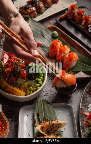 Du haut de la crop-personne avec des baguettes mangeant des sushis avec du saumon et des herbes d'une table avec différents plats d'un restaurant asiatique de luxe Banque D'Images